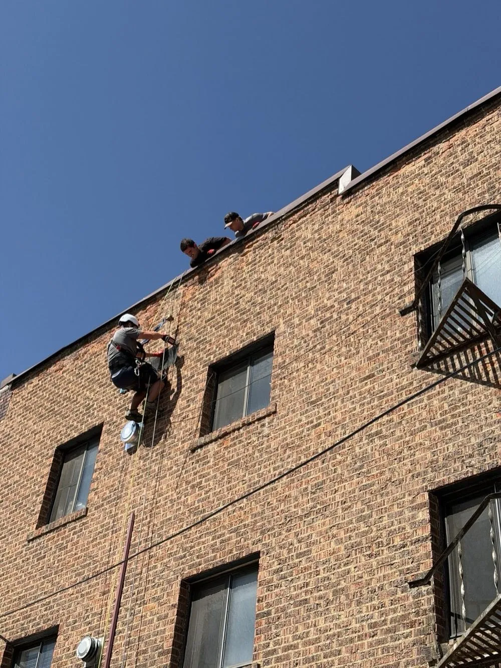 Rope access team working on the upper wall of a brick apartment building